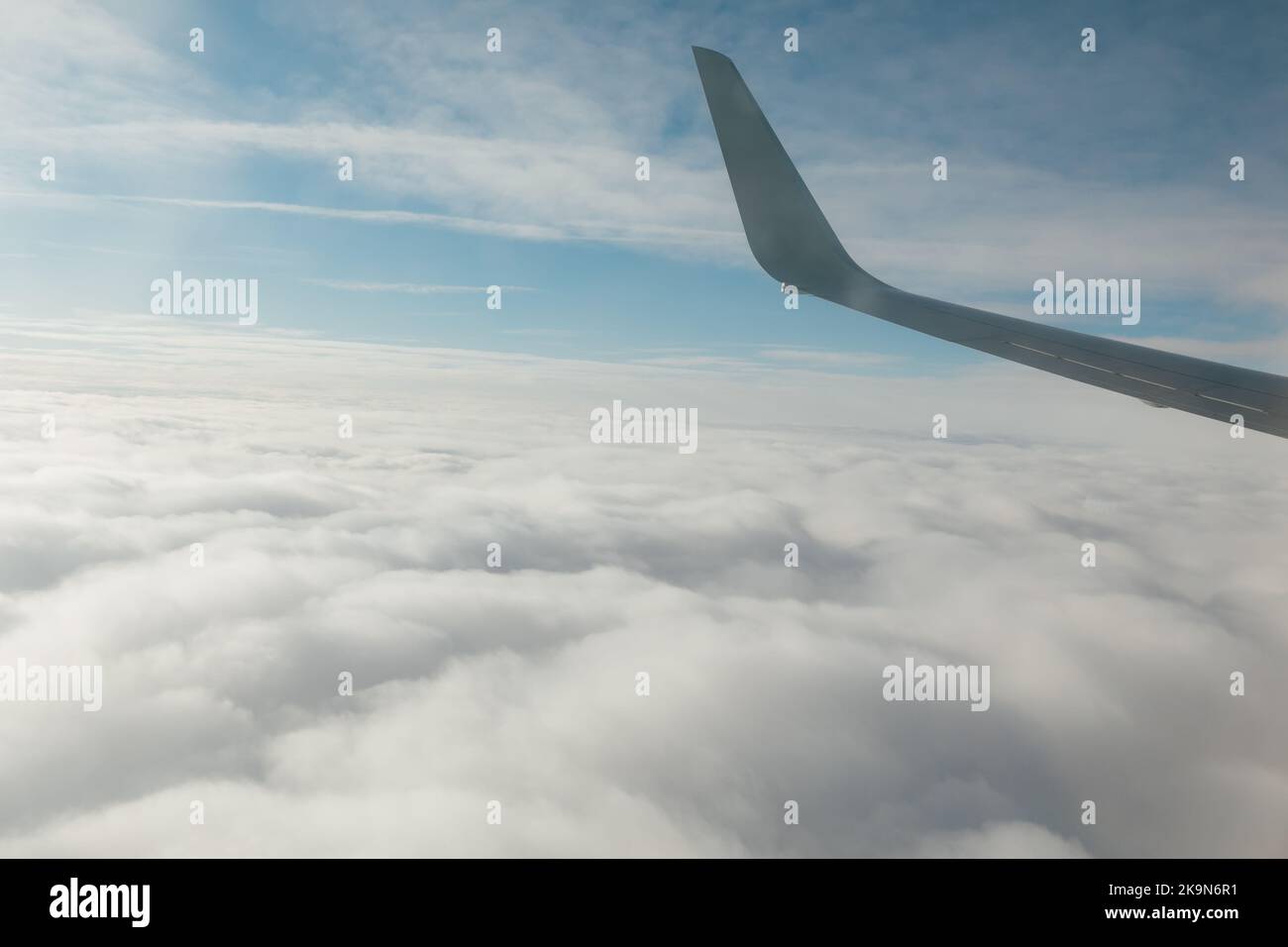 wing of an airplane in flight above clouds in a blue sky Stock Photo ...