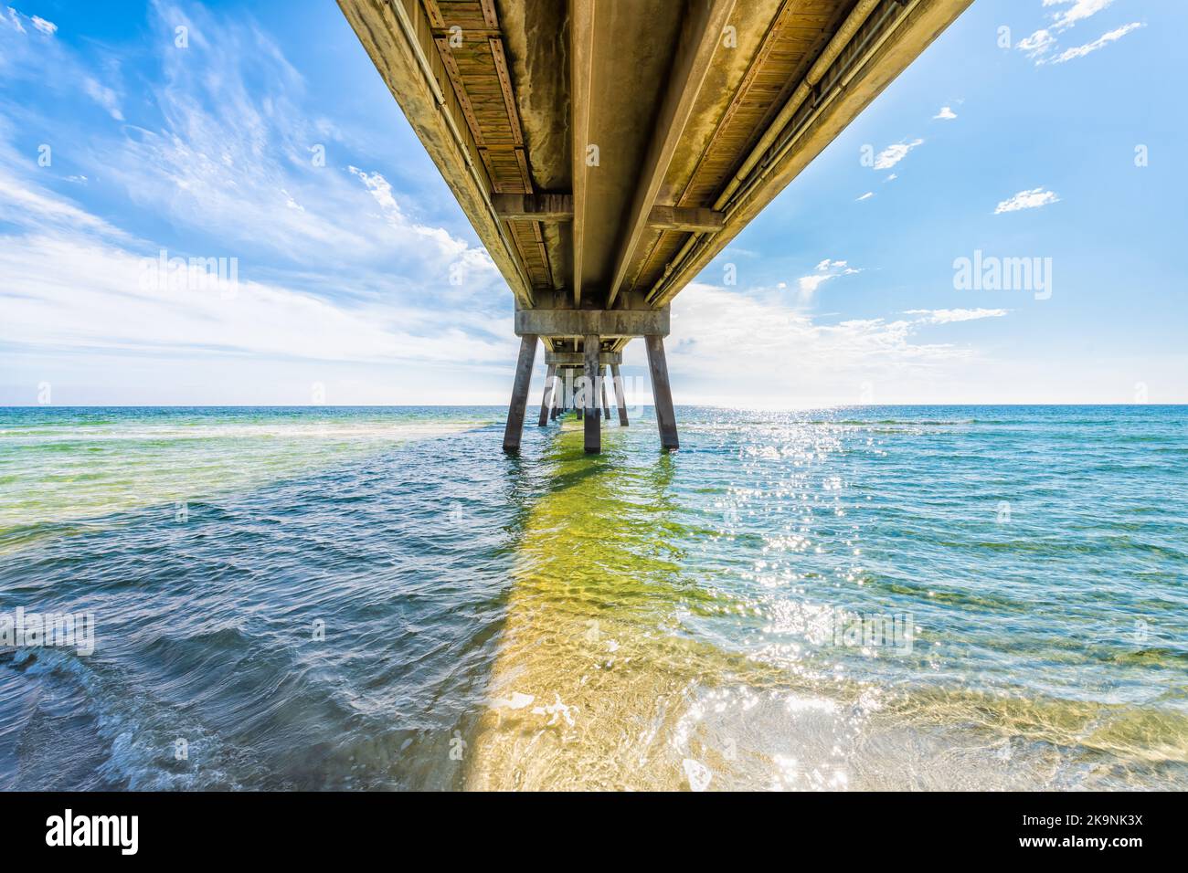 Under Okaloosa island fishing pier, Fort Walton Beach, Florida panhandle with wooden pillars, waves in Gulf of Mexico with sun path water reflection Stock Photo