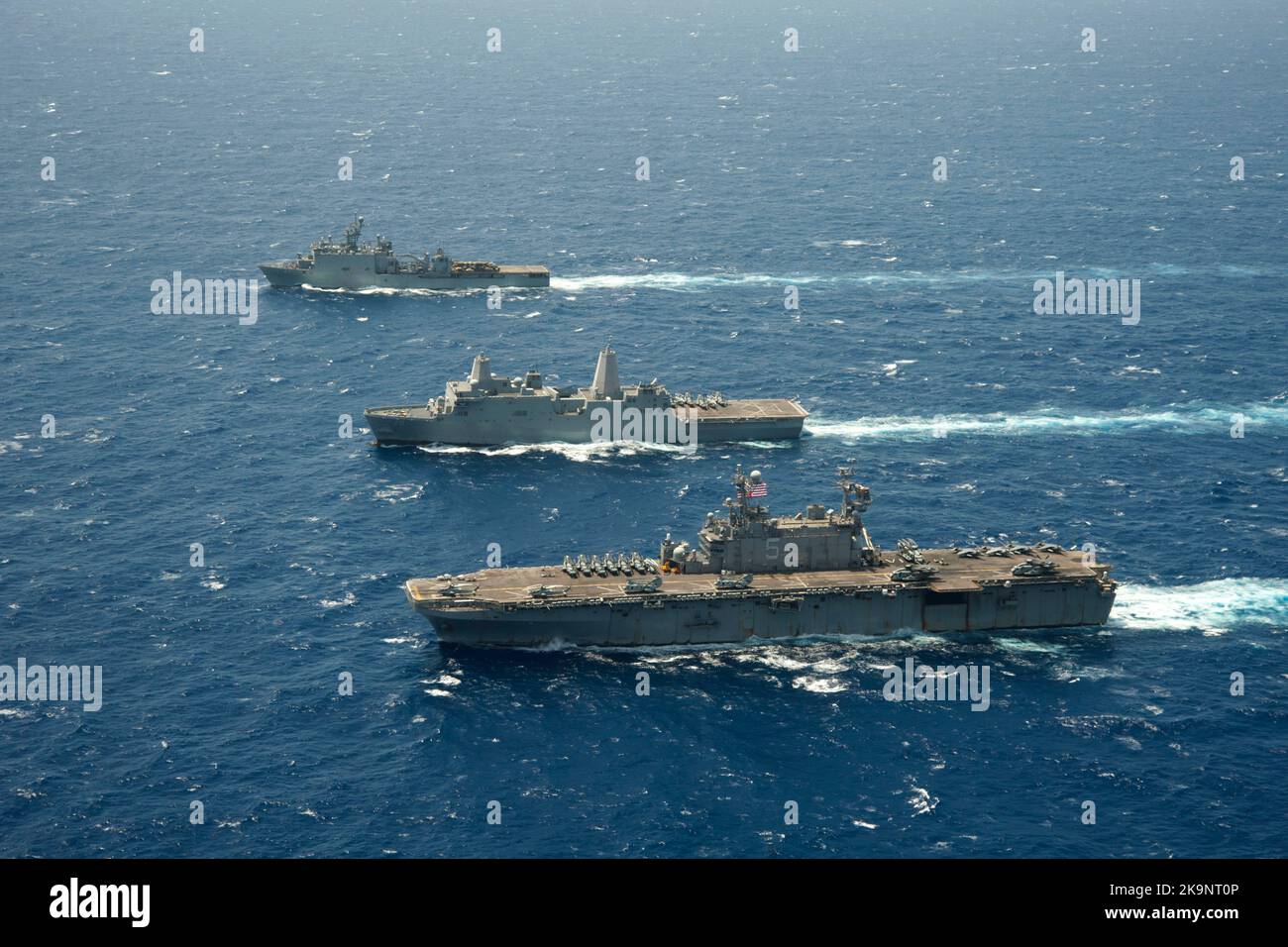 The amphibious assault ship USS Peleliu (LHA 5) transits the Pacific Ocean with the amphibious transport dock ship USS Green Bay (LPD 20), middle, and the amphibious dock landing ship USS Rushmore (LSD 47). Stock Photo