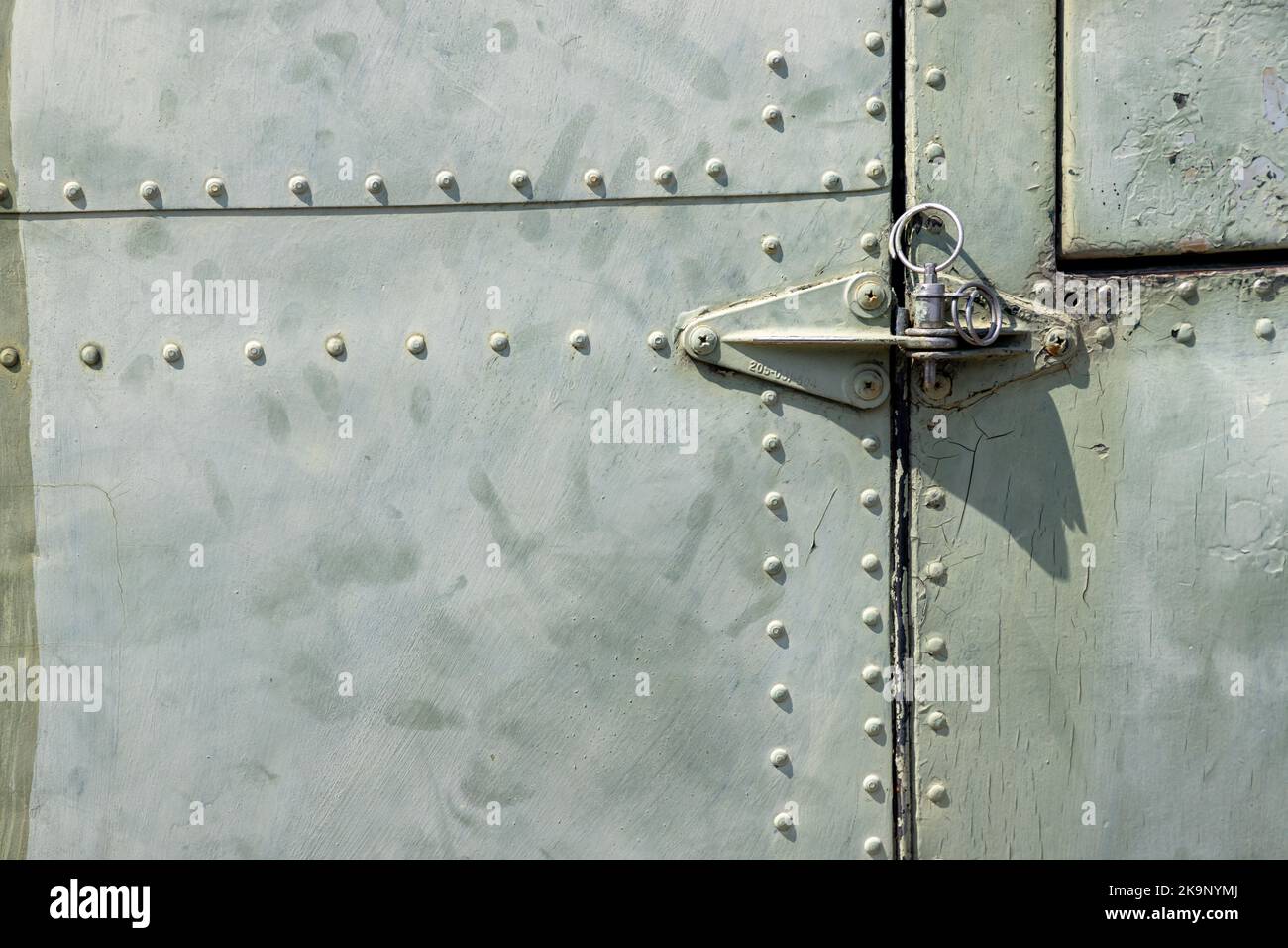 The exterior wall surface of a very old military green military helicopter. There is a door hinge on the right side of the picture. in the bright sunl Stock Photo