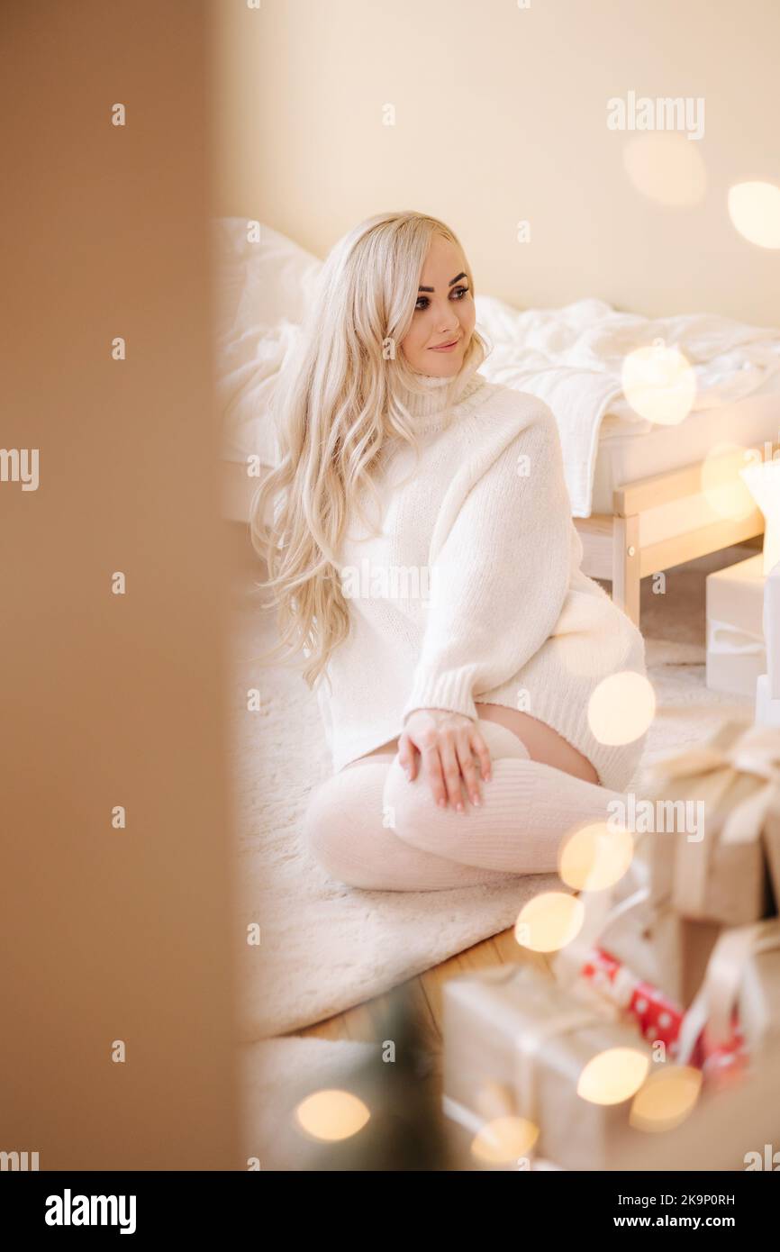 Portrait of Beautiful blond hair woman in pullover open present on Chrisrmas time. Elegant woman by Christmas tree. Attractive female hold present Stock Photo