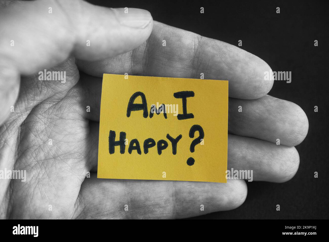 A man holding a yellow piece of paper with the question Am I Happy written on it in the palm of his hand. Close up. Stock Photo