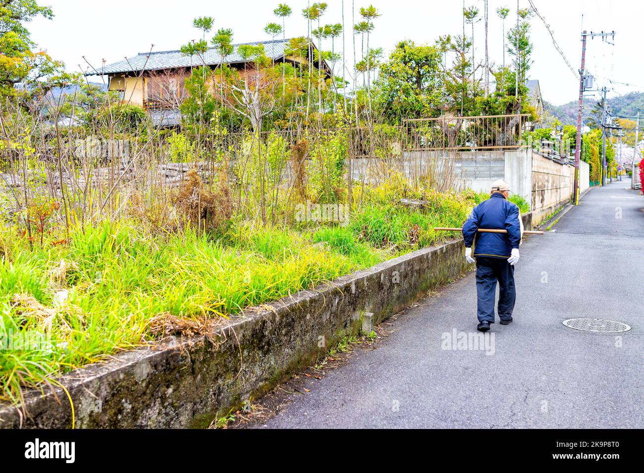 Kyoto, Japan - April 11, 2019: Senior elderly man walking with wooden stick behind back exercise in residential neighborhood with houses and garden Stock Photo