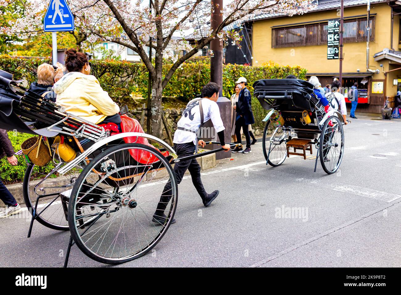 Kyoto, Japan - April 11, 2019: Arashiyama Togetsukyo Bridge street with people tourists riding rickshaw tour walking by cherry blossom trees in spring Stock Photo