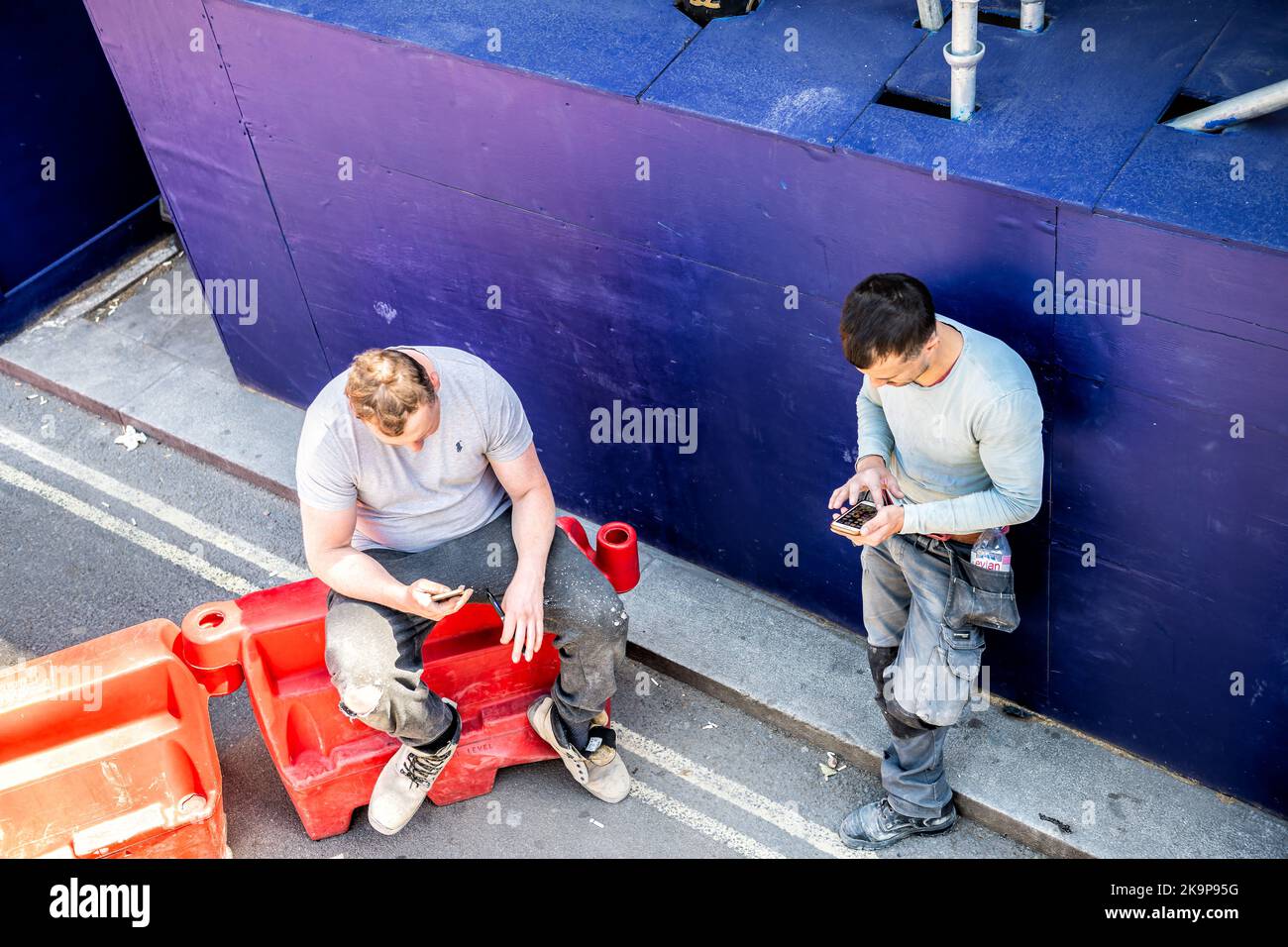London, United Kingdom - June 22, 2018: Two construction workers men taking lunch break, using phones outside on street of city of Westminster Stock Photo