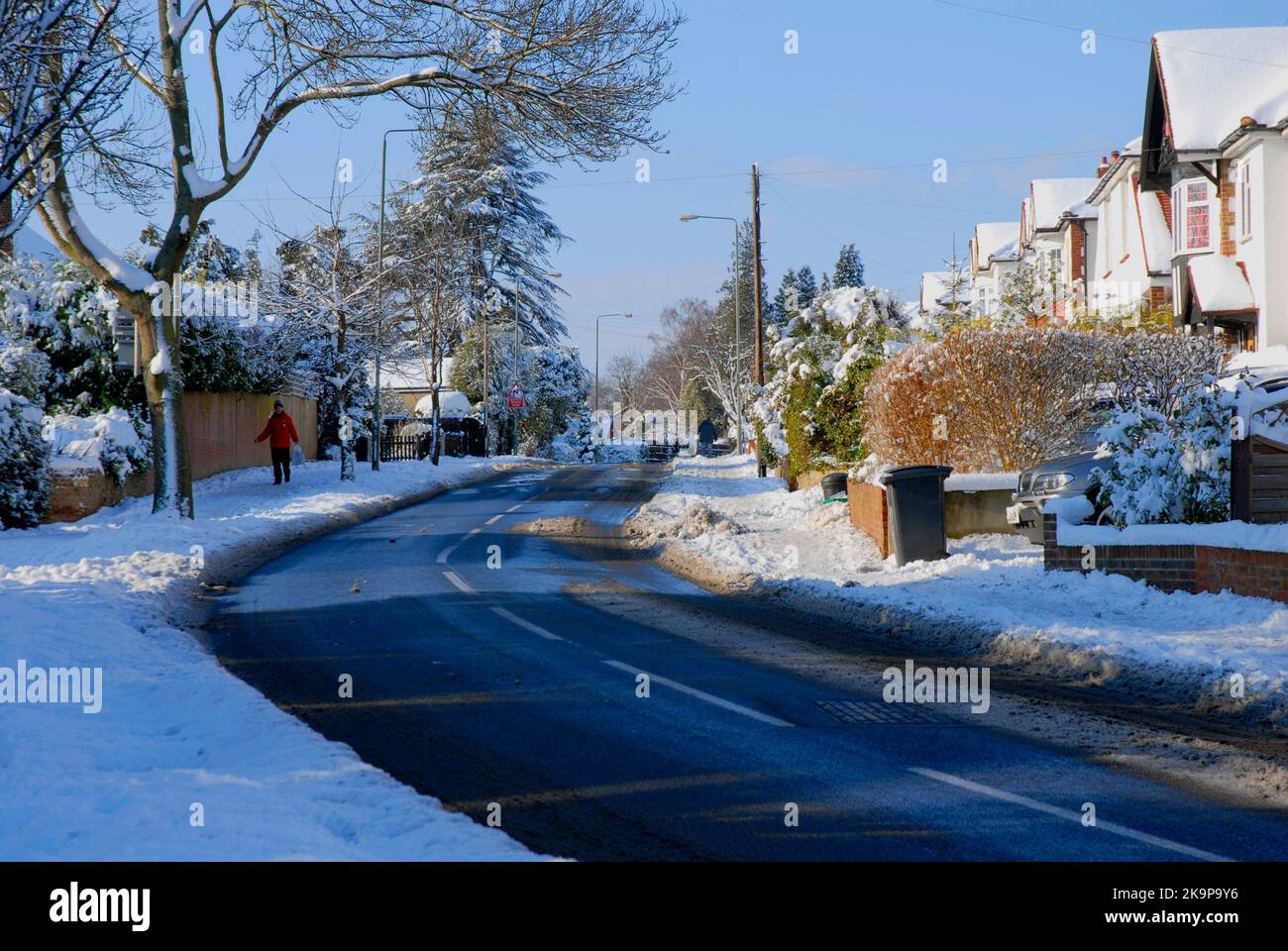 A curved, residential suburban street after snowfall, with the snow on the road surface turning to slush and pedestrians walking with great care Stock Photo