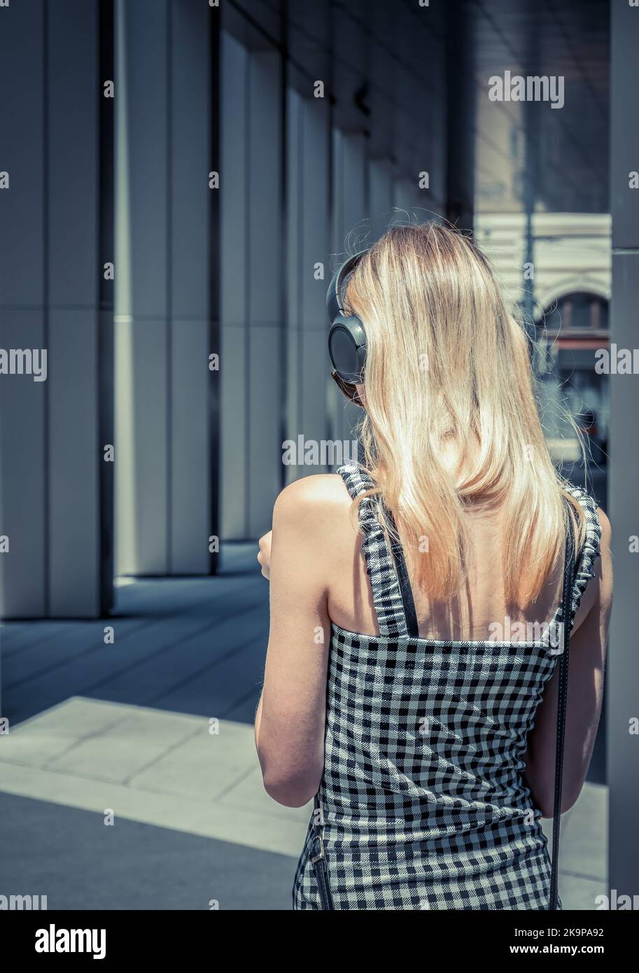 Rear view of a young blonde woman wearing over the ear headphones. Girl ...