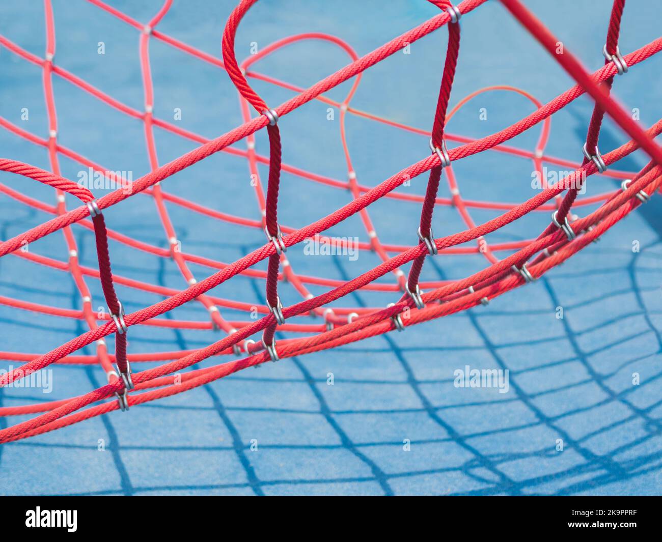 Red net on blue background. Sport equipment on public sportsground in sunny day. Geometrical shadows in sunny day. Stock Photo