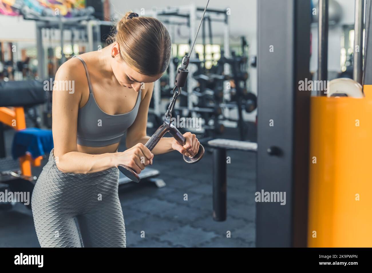 Medium indoor shot of strong determined caucasian skinny girl in her 20s wearing stylish gray sportswear exercising at gym, using weight lifting machine. High quality photo Stock Photo