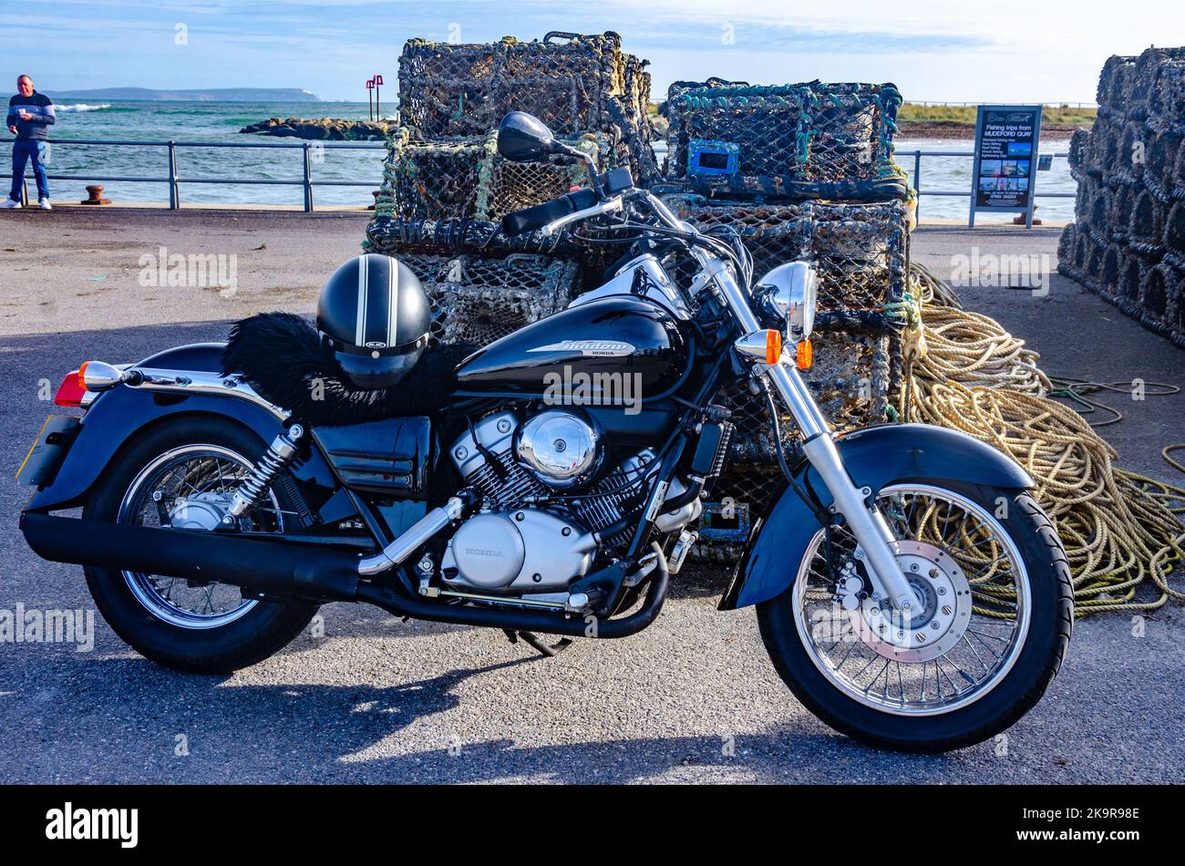 A black Honda Shadow motorbike parked in front of piles of ropes and lobster pots on the quayside at Mudeford near Christchurch in Dorset, UK Stock Photo