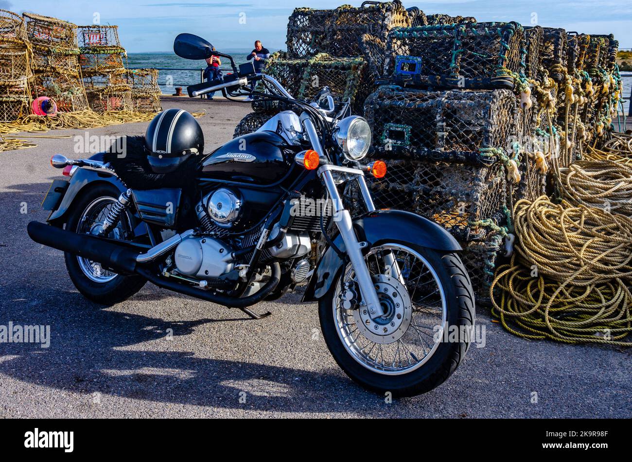 A black Honda Shadow motorbike parked in front of piles of ropes and lobster pots on the quayside at Mudeford near Christchurch in Dorset, UK Stock Photo