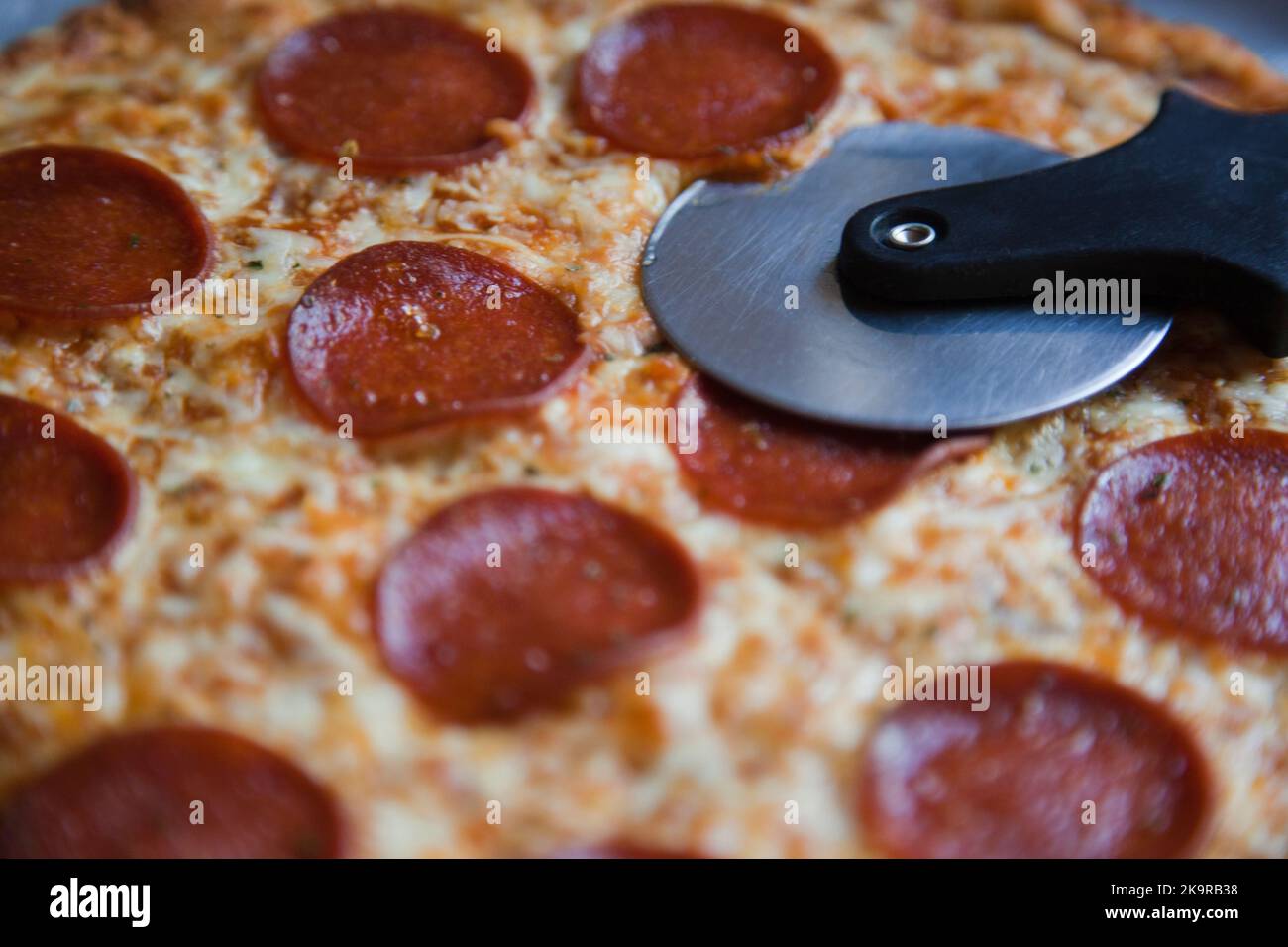Baked pepperoni and cheese thin crust pizza with a pizza cutter Stock Photo