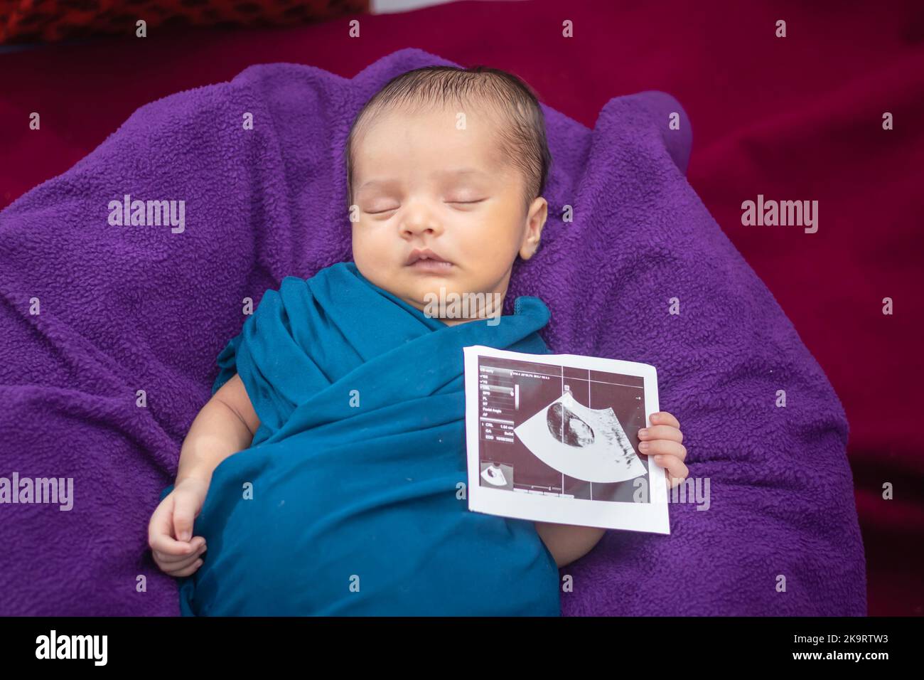 newborn baby holding ultrasound copy in hand and sleeping in baby wrap Stock Photo