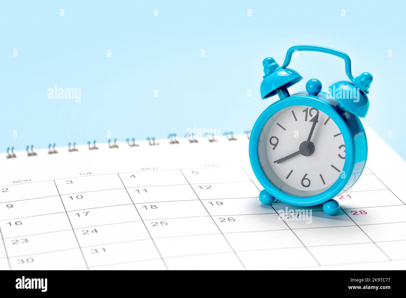 Blue alarm clock on a calendar with a blue background. Stock Photo