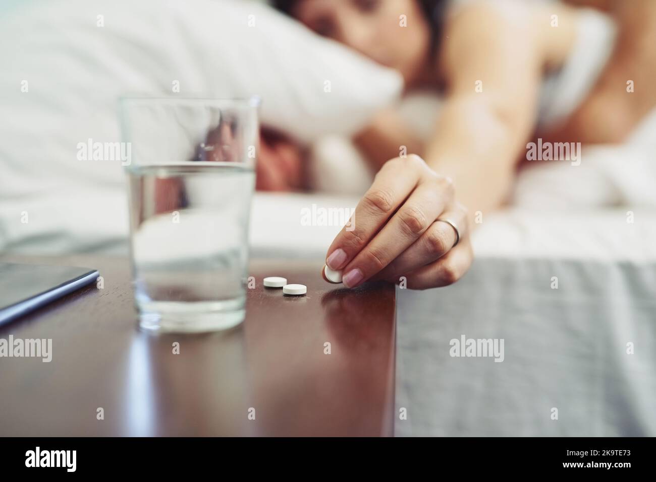 Goodbye headache. an unrecognizable woman lying in bed and taking a pill to drink after waking up sleeping in bed. Stock Photo