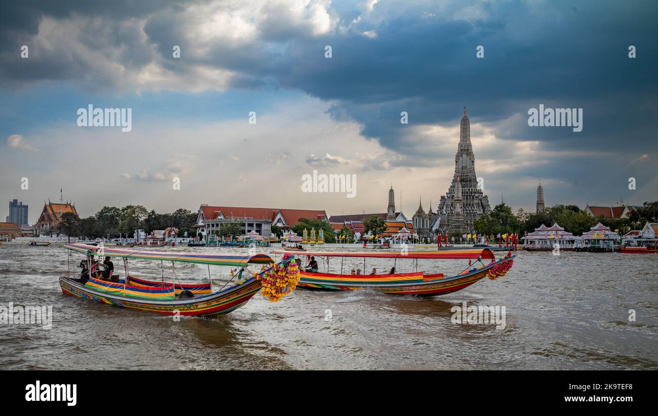 Traditional long tail boats for tourist trips move down the Chao Phraya River opposite Wat Arun, or The Temple of Dawn, in Bangkok, Thailand. Stock Photo