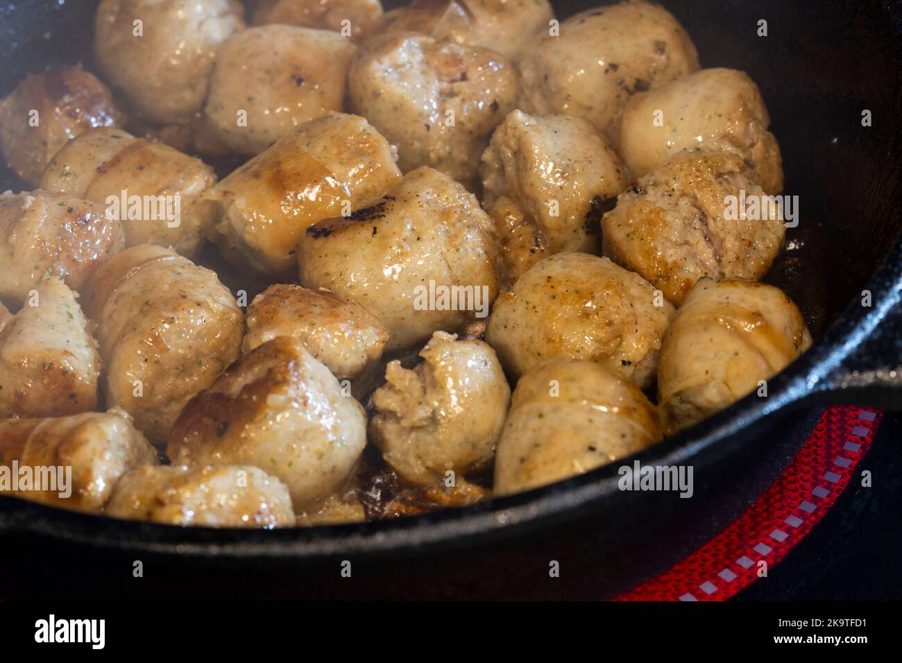 Frying pork sausage meat balls, with olive oil, in a cast iron frying pan, on an electric hob stove Stock Photo