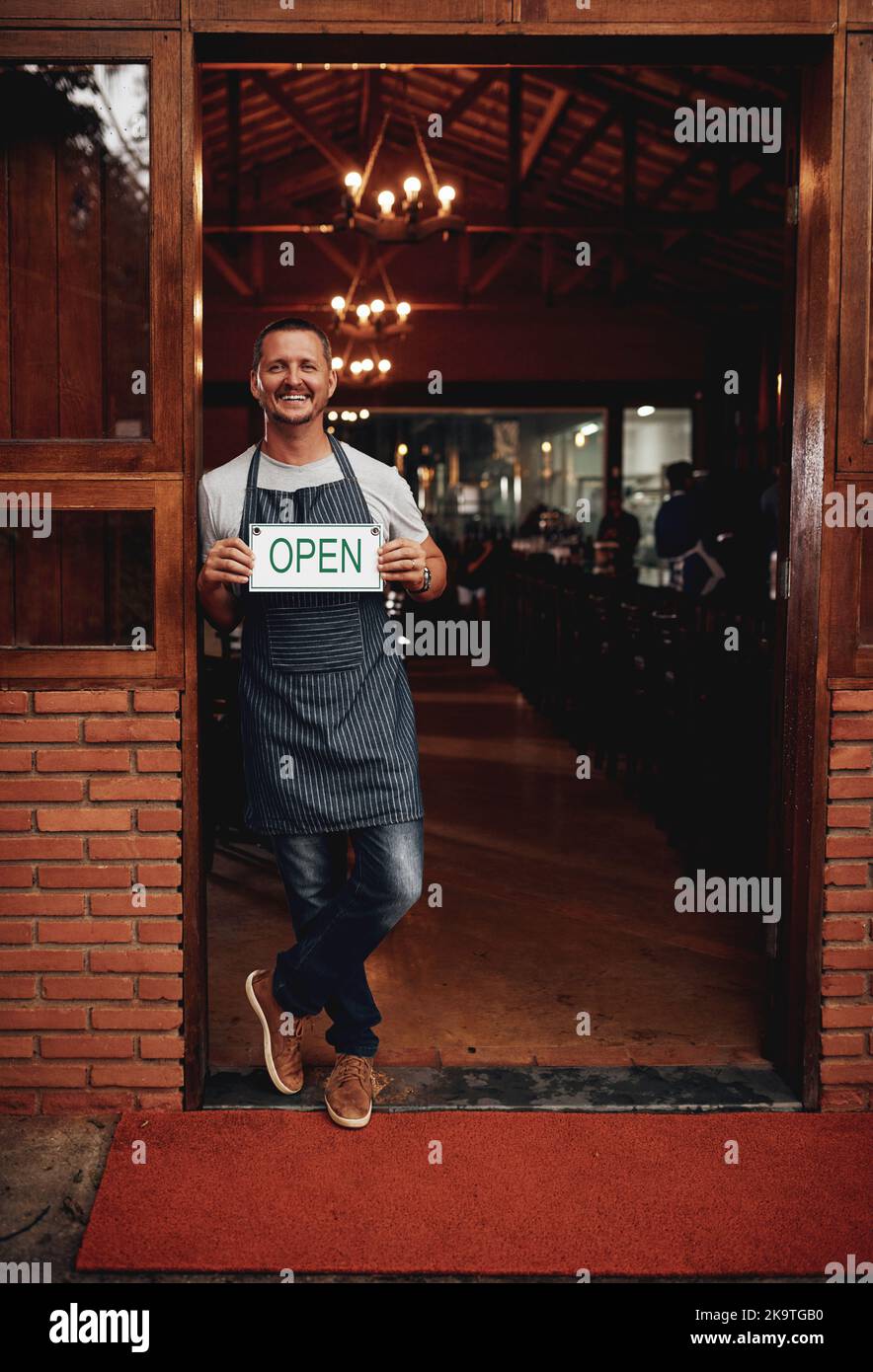 We have everything you will need here. Portrait of a cheerful middle aged business owner holding up a sign saying open while standing under a doorway Stock Photo