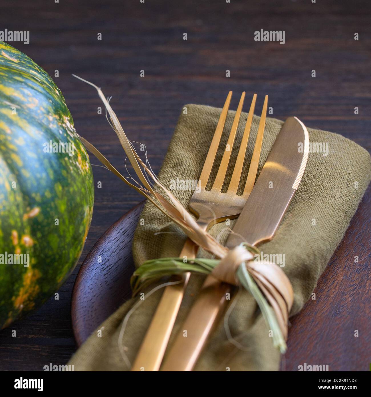 Gold cutlery with napkin and pumpkin on wooden table for Thanksgiving dinner concept. Festive autumn table settings background. Stock Photo
