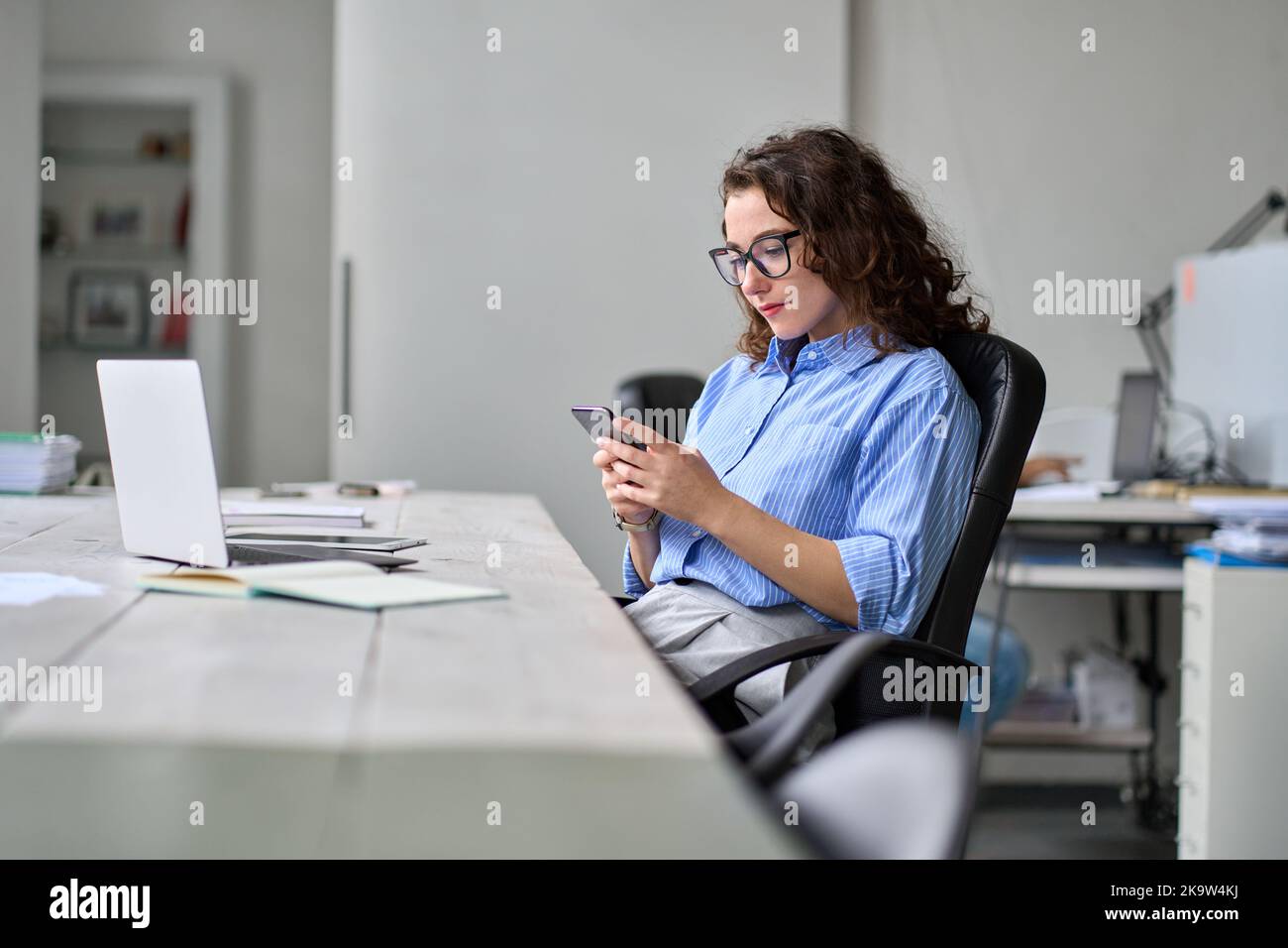 Young business woman using smartphone working in office sitting at desk. Stock Photo