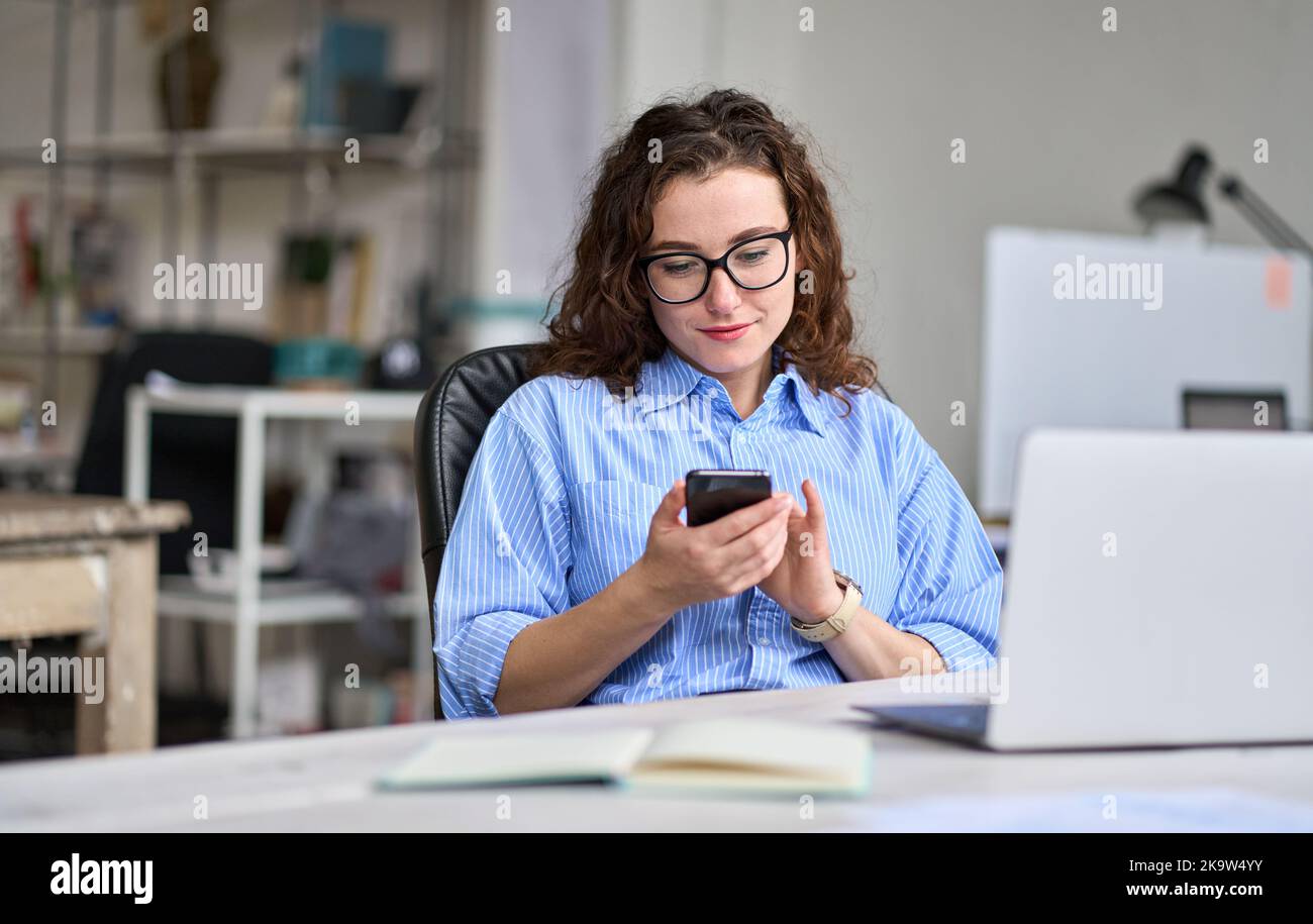 Young business woman using mobile phone working in office sitting at desk. Stock Photo