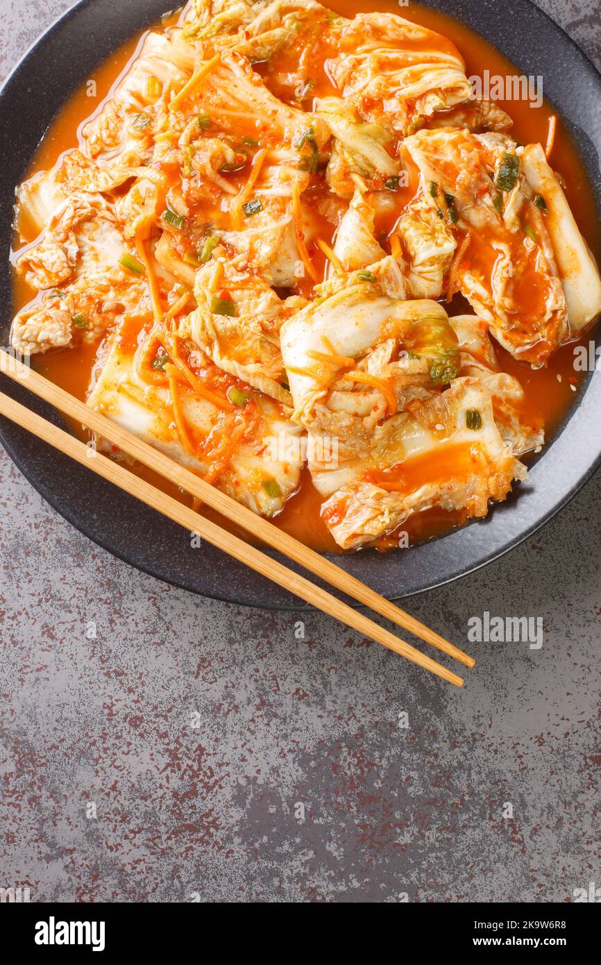 Korean Food Traditional Kimchi napa cabbage with carrot, daicon, onion, garlic and spice closeup in a black dish on a table. Vertical top view from ab Stock Photo