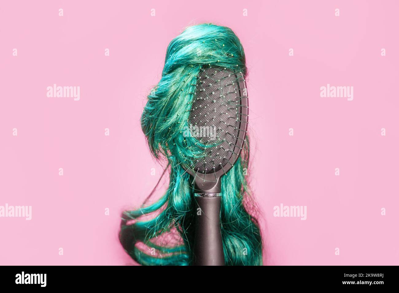 Hair coloring and dye. Comb with turquoise wig on pink background, like woman's head. Hairstyle and beauty salon. Copy space. Concept of hair care, ba Stock Photo