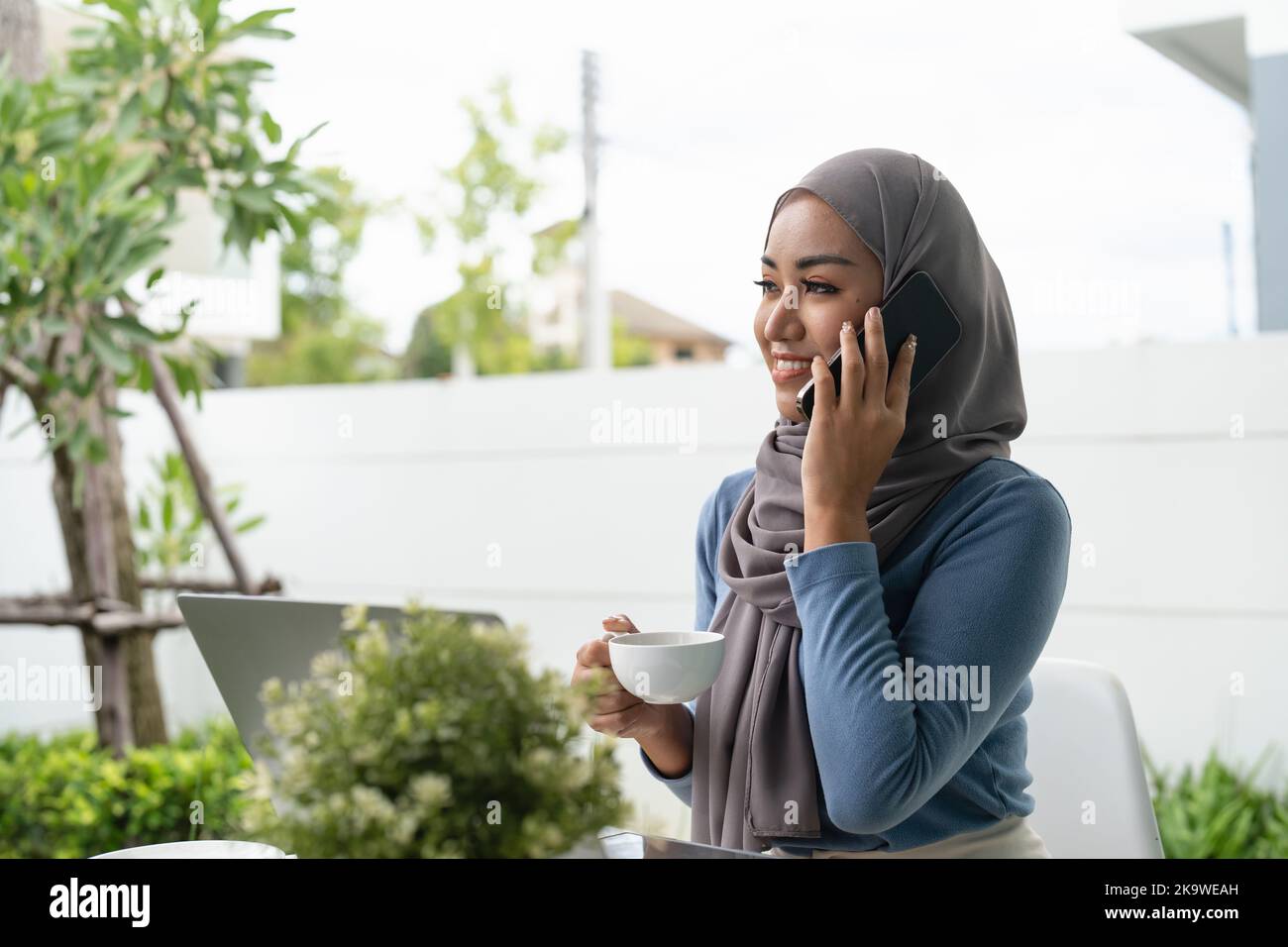 Portrait of Muslim asian woman in hijab using laptop while taking call ...