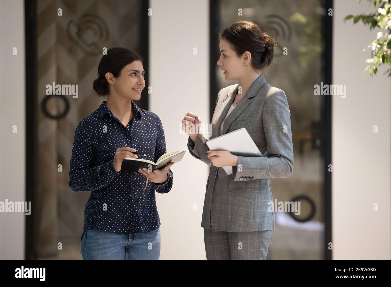 Two multi ethnic businesswomen standing in office hallway and talking Stock Photo