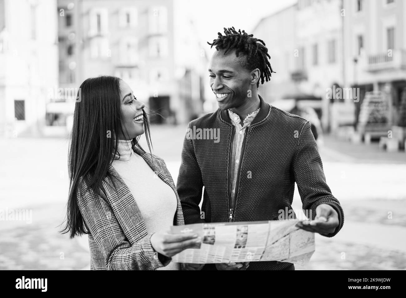 Happy african couple having fun looking city map during travel vacation - Focus on woman face - Black and white editing Stock Photo