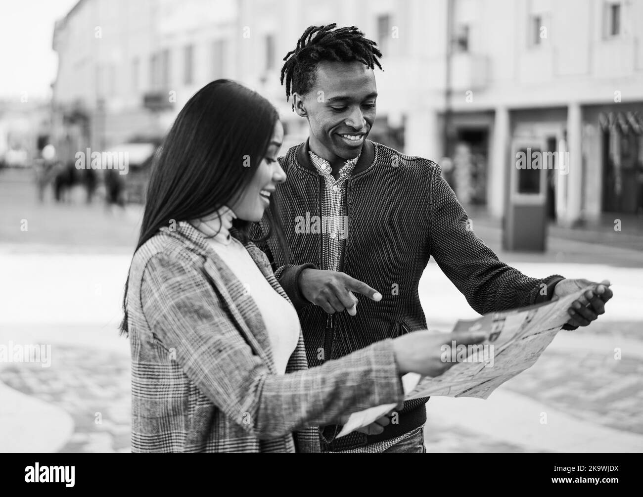 Happy african couple having fun looking city map during travel vacation - Focus on man face - Black and white editing Stock Photo