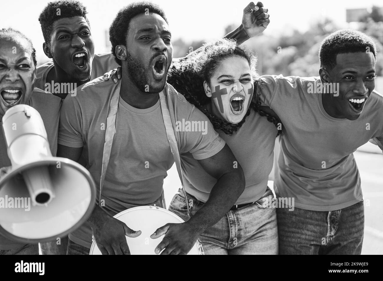 African sport fans screaming while supporting their team - Football supporters having fun at competition event - Black and white editing Stock Photo