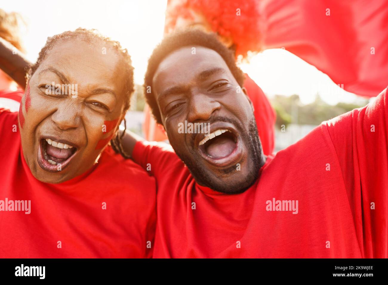 African red sport fans screaming while supporting their team - Football supporters having fun at competion event - Champions and winning concept - Foc Stock Photo