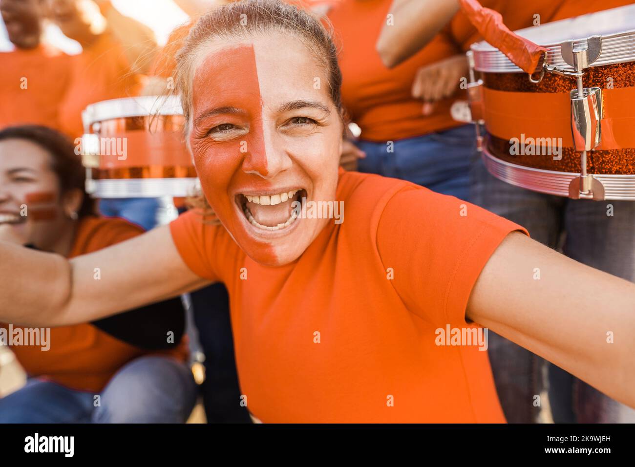 Orange sport fans screaming while supporting their team - Football supporters having fun at competition event - Focus on senior woman face Stock Photo
