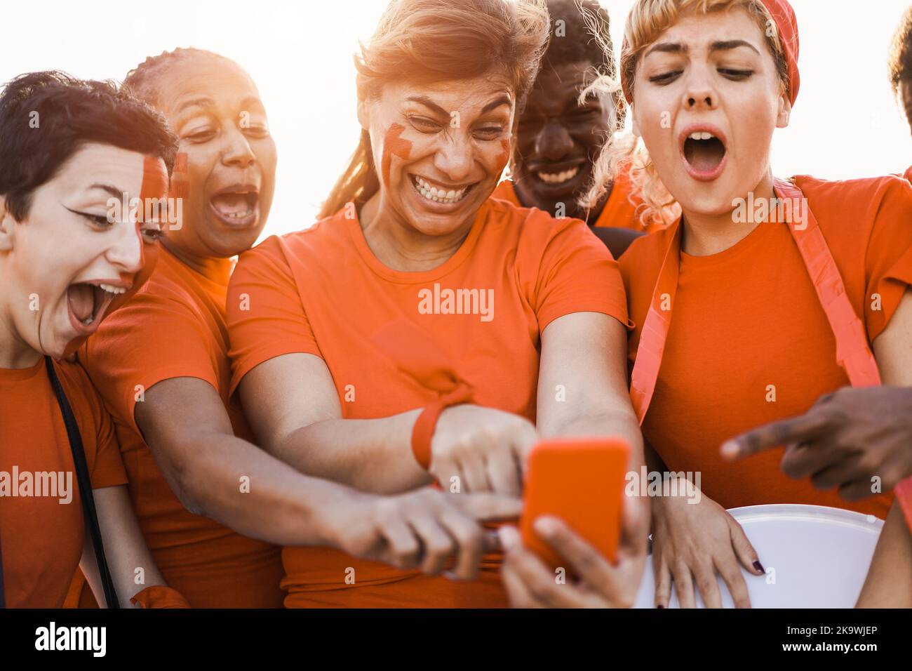 Orange sport supporters watching football game on mobile phone - Focus on center woman face Stock Photo