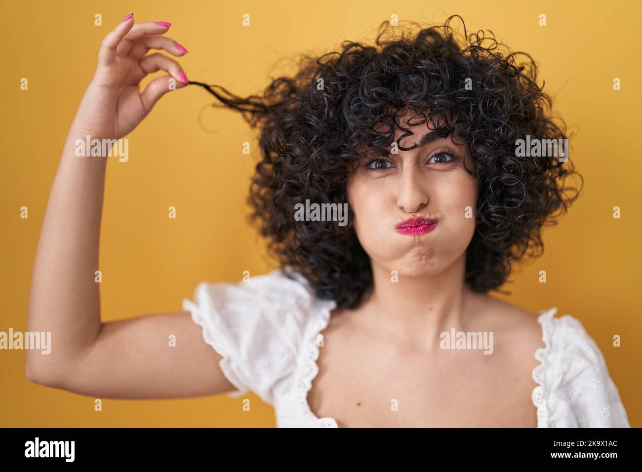 Young brunette woman with curly hair holding curl puffing cheeks with funny face. mouth inflated with air, catching air. Stock Photo