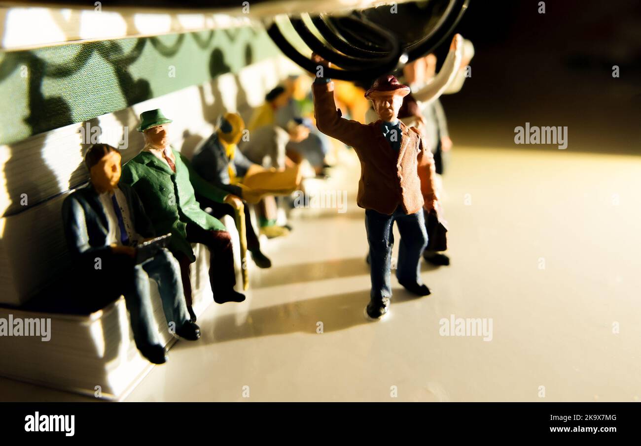 Miniature toy of people travelling from work on a public transport concept with evening yellowish side lighting - travel on a train or bus. Stock Photo