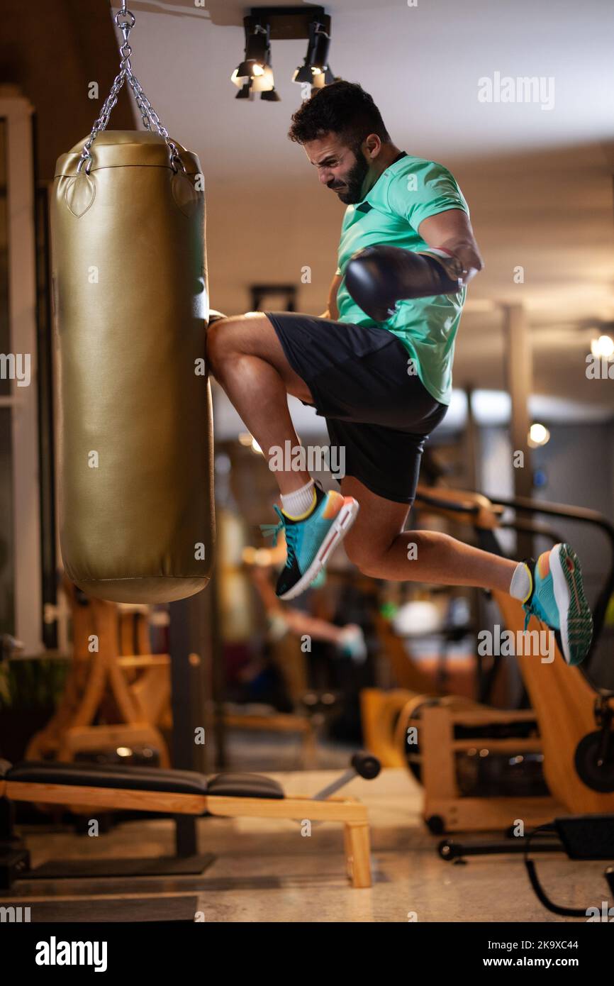 Muscular man with boxing gloves jump hitting a punching bag with a knee