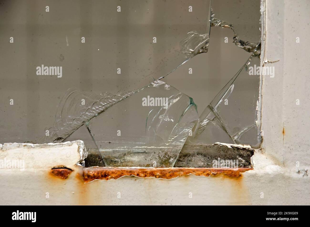 Damage in the corner of a window with rust on the frame and cracks in