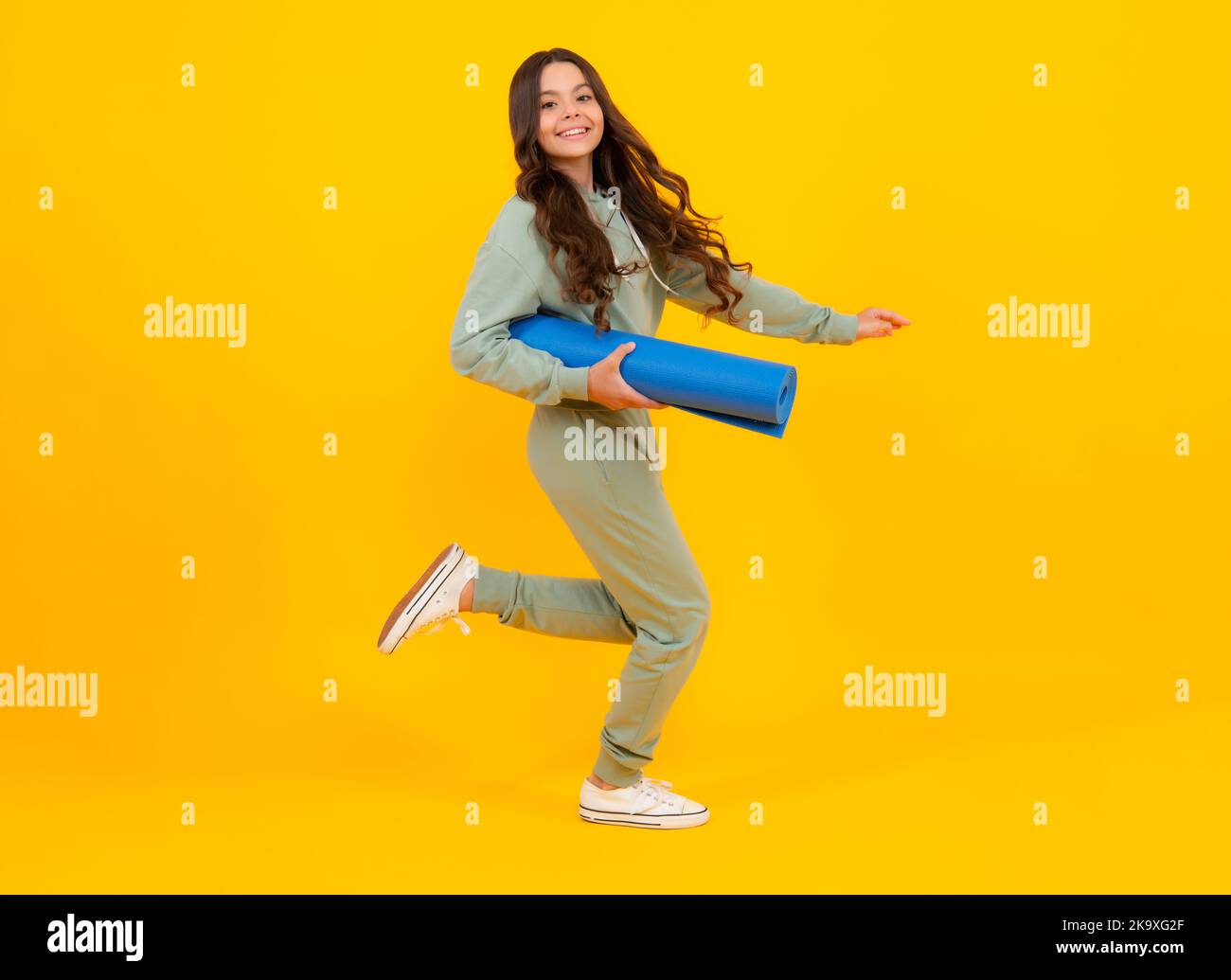 Sportswear advertising concept. Teenager child girl in tracksuits jogging suit posing in the studio hold fitness mat. Run and jump. Stock Photo