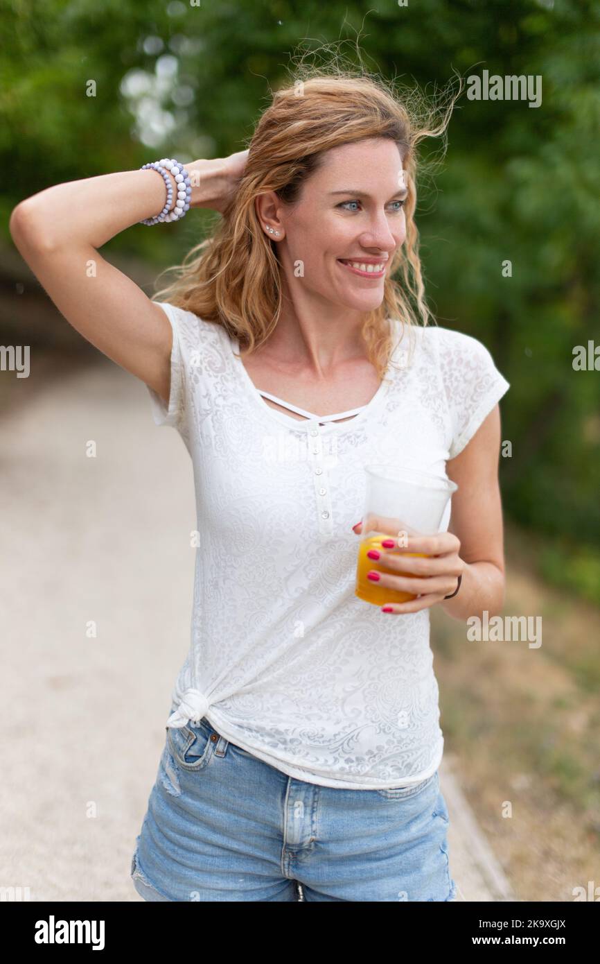 Happy young Caucasian 30s woman holding glass of juice in nature and