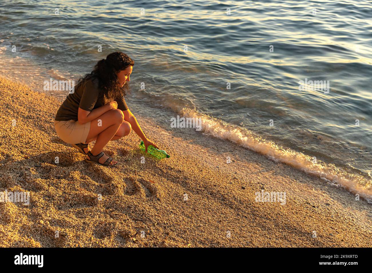 Earth day. Cleanup garbage on the Adriatic sea coast. A girl picking up a plastic bottle on the beach. Sunset. The concept  of conservation of ecology Stock Photo