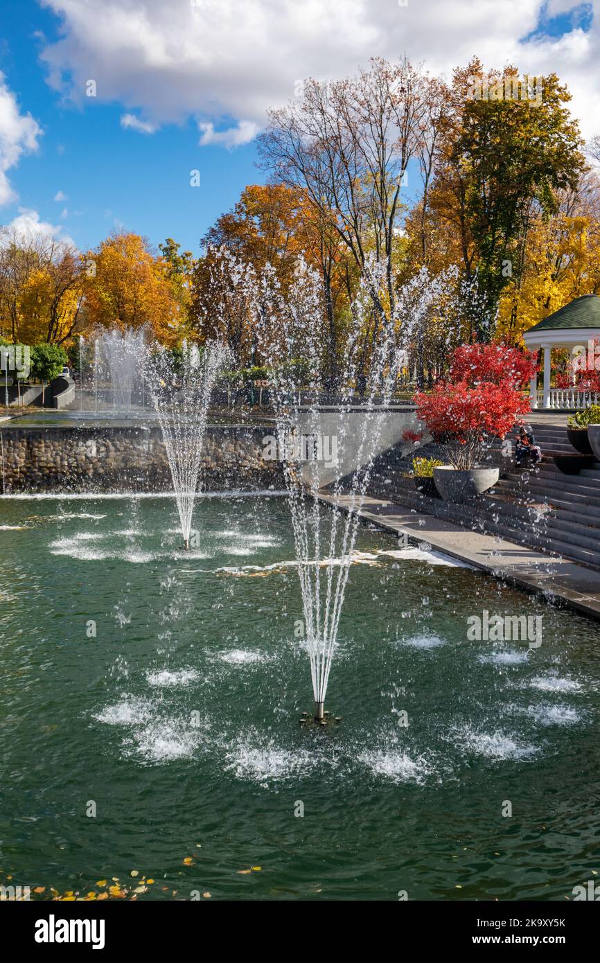 Red autumn tree branches and fountains in recreation area in Shevchenko City Garden. Tourist attraction in central city park, Kharkiv Ukraine Stock Photo