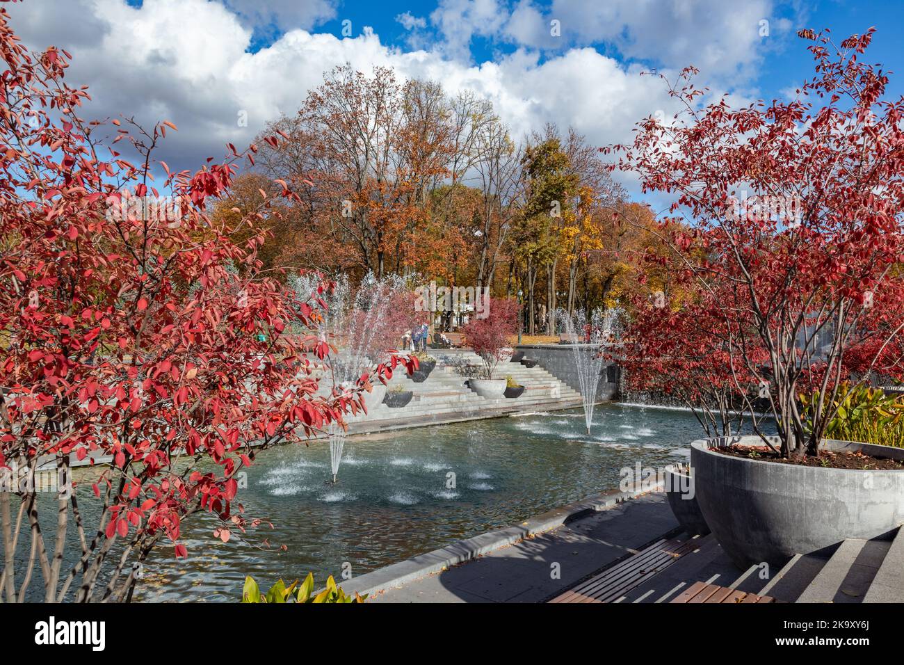 Red and golden autumn trees with fountains in recreation area in Shevchenko City Garden. Tourist attraction in city park, Kharkiv Ukraine Stock Photo