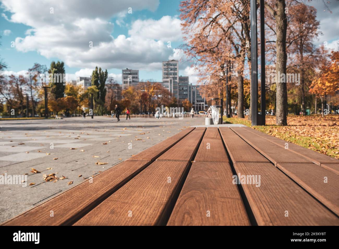 Bench close-up with autumn city park background. Modern recreation area with fountain near Derzhprom constructivist building in Kharkiv, Ukraine Stock Photo