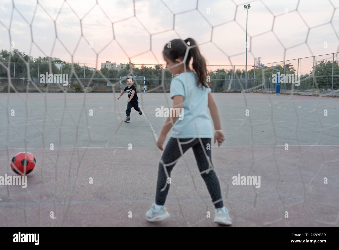 Young girl soccer goalkeeper warding the football goal. Child running for ball in soccer field. Selective focus on boy. Stock Photo