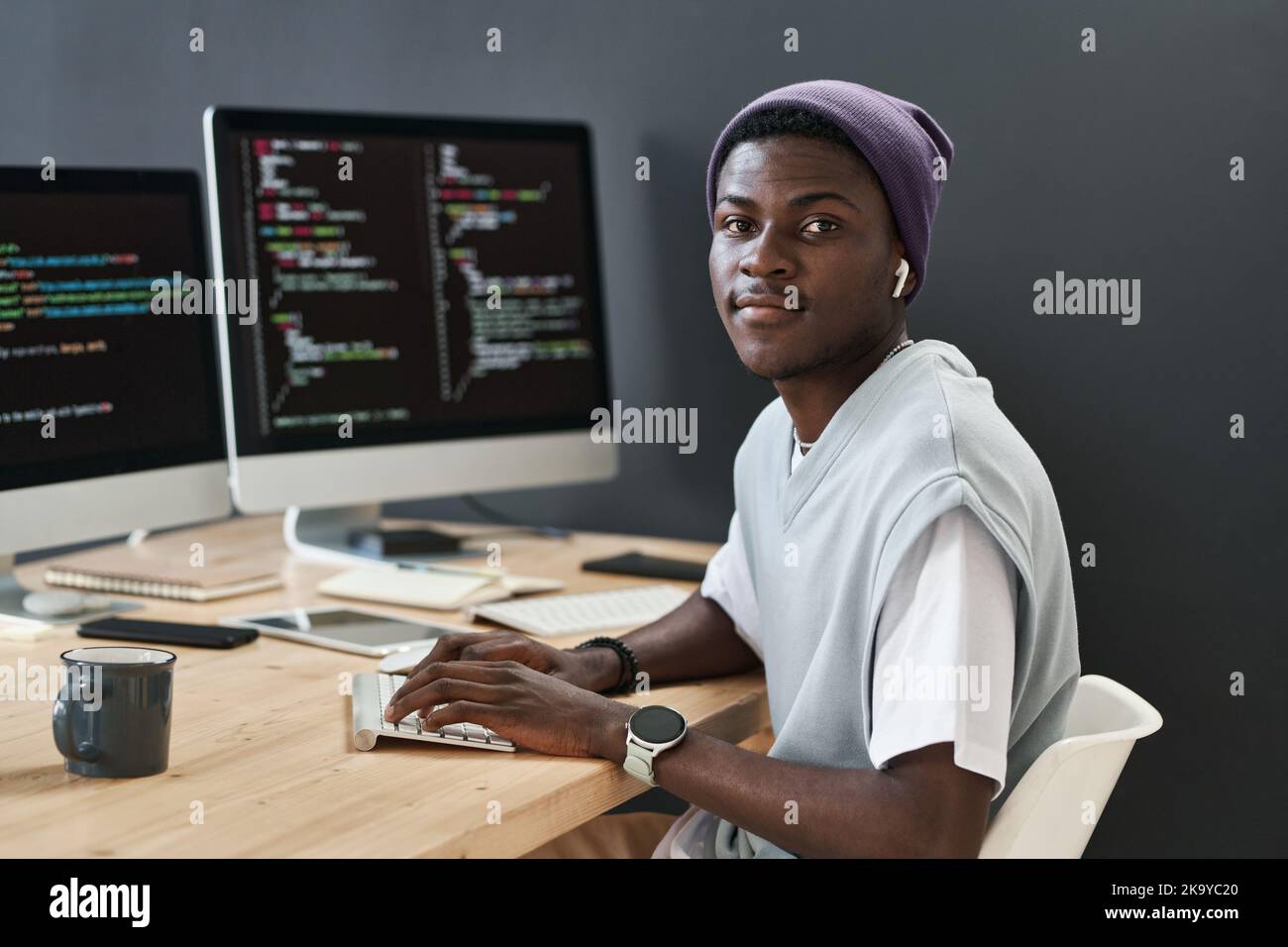 Young confident African American IT support manager looking at camera while sitting by workplace in front of computer monitors Stock Photo