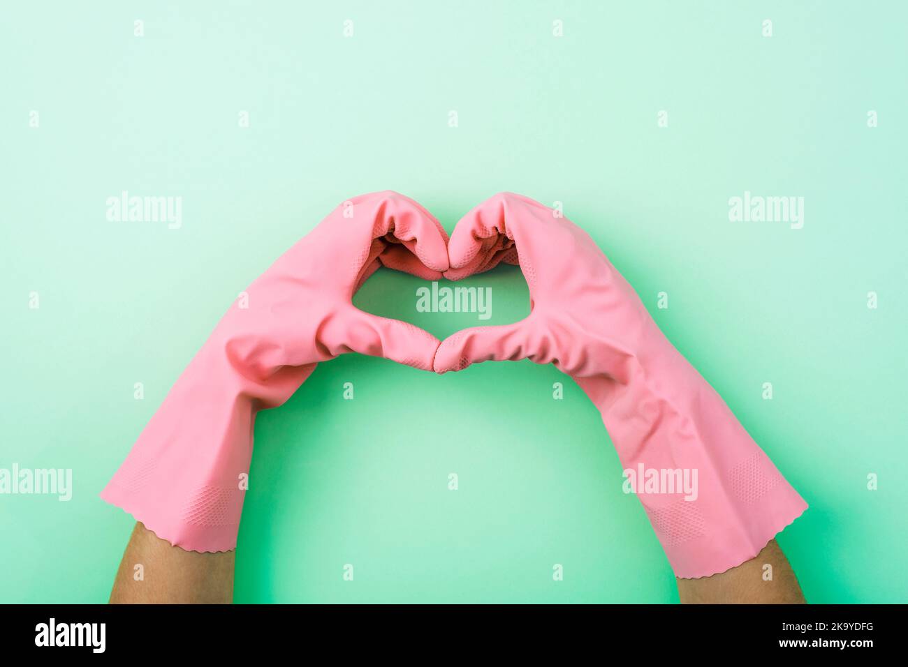Heart shaped hands in pink rubber gloves on green background. House