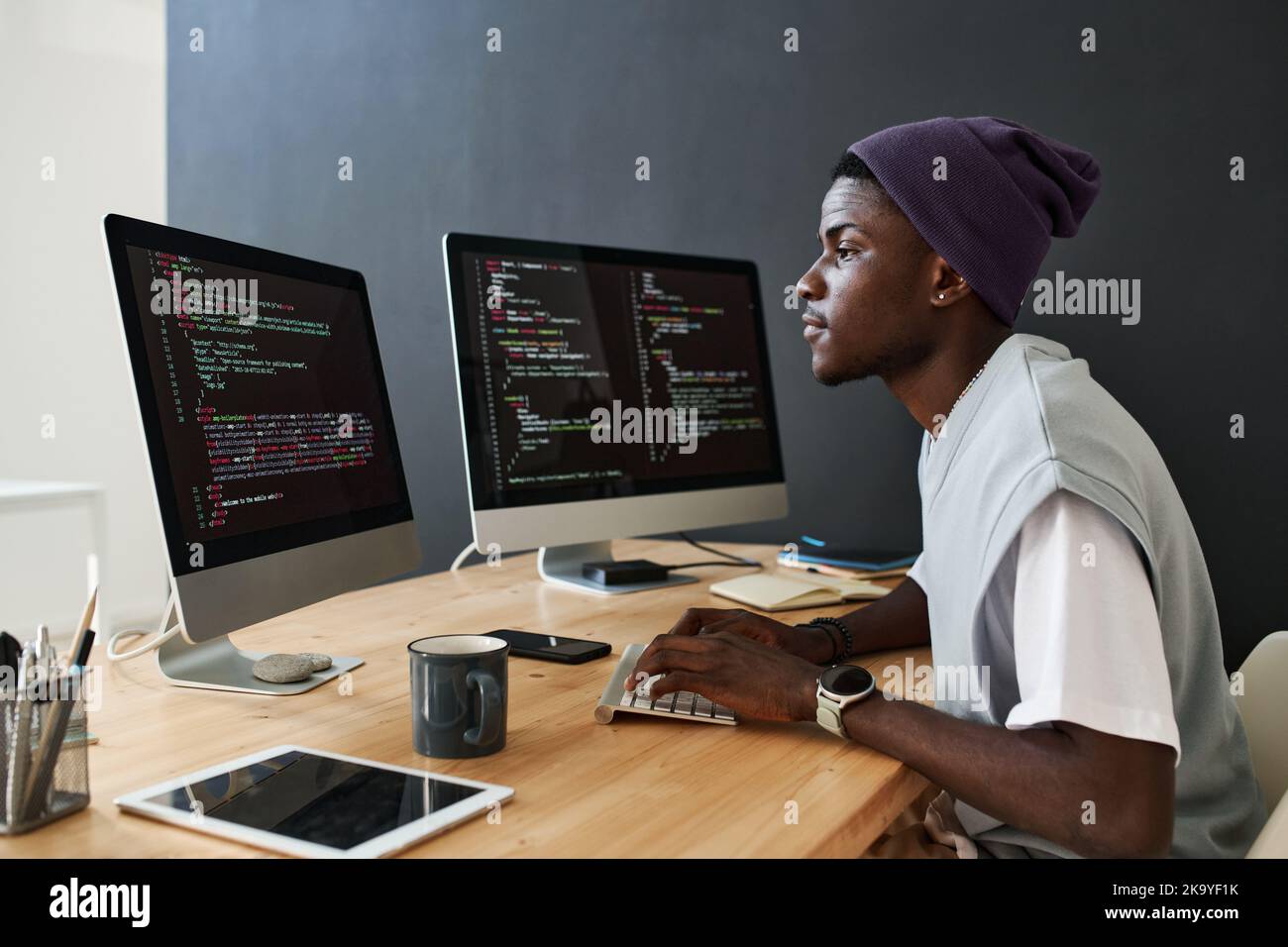 Young serious African American male programmer working over new software in front of computer screens with coded data in office Stock Photo