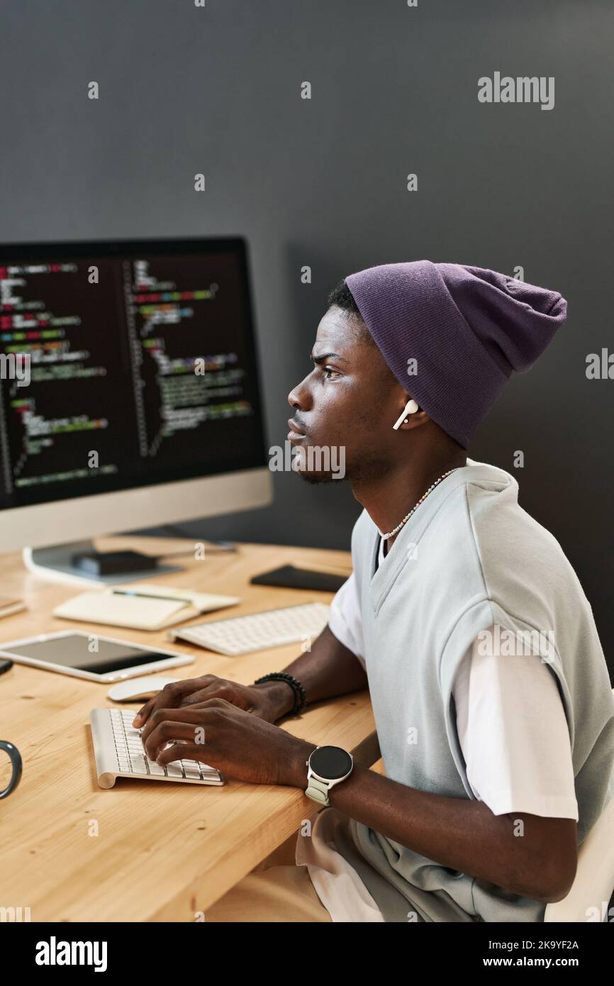 Young serious IT engineer with earphones looking at one of computer ...